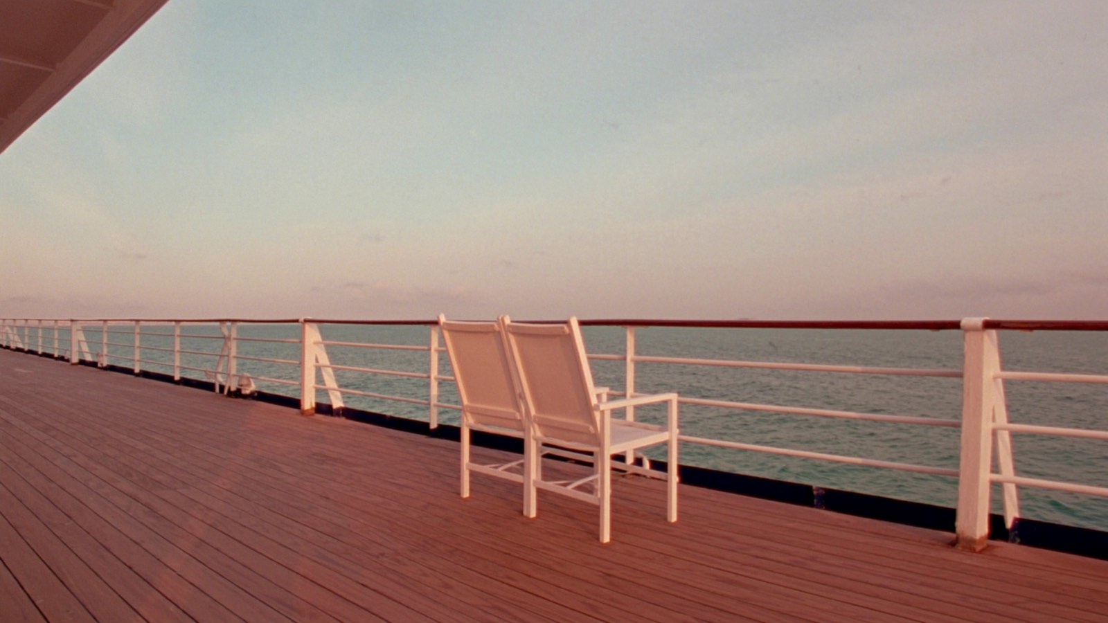 Two empty deck chairs on a ship deck at golden hour