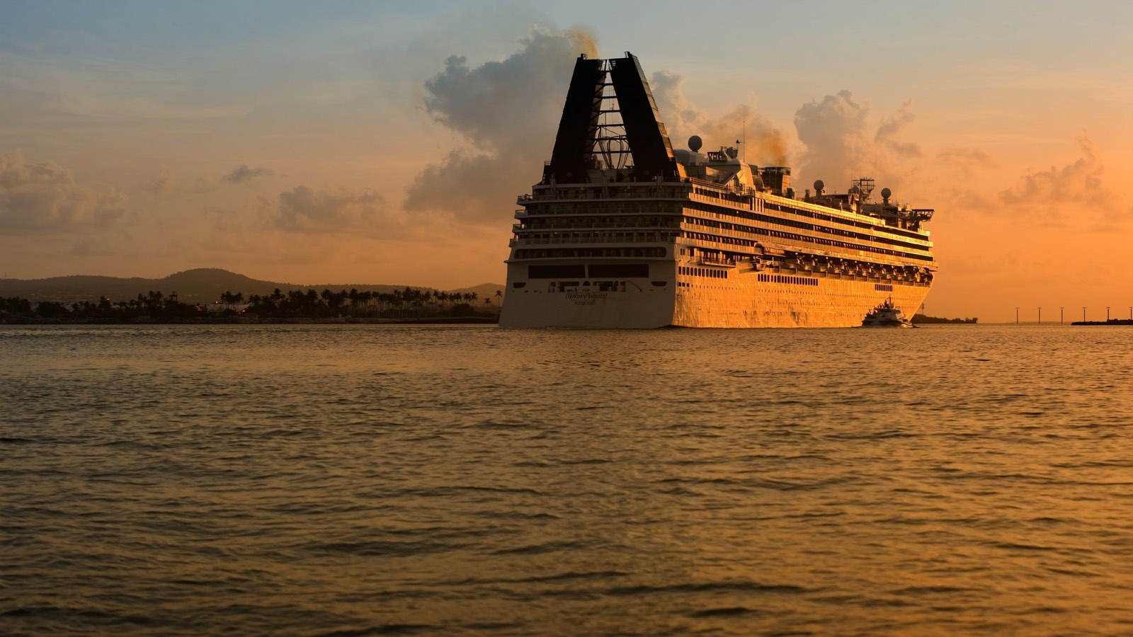 A cruise ship leaving a tropical port at sunset