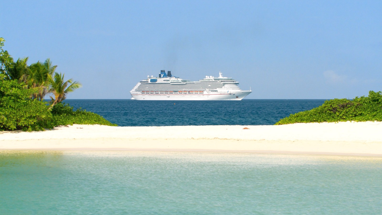 A large white cruise ship anchored off a tropical island