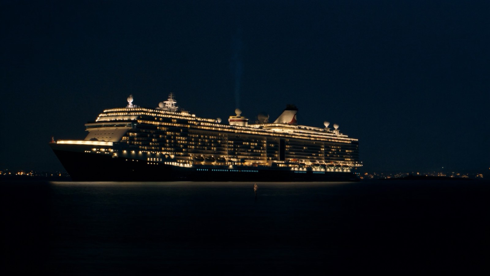 A large cruise ship lit up at night on dark water