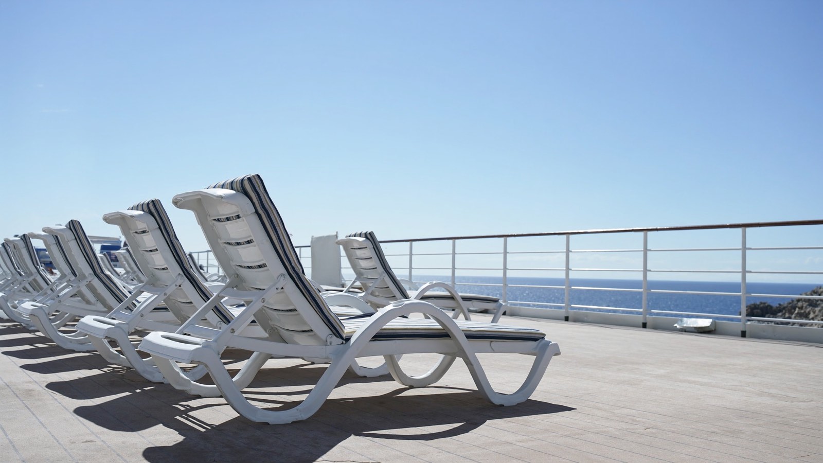 An empty sun deck lined with loungers under a clear sky